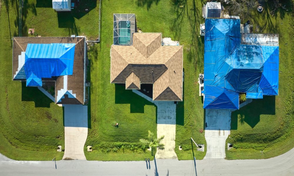 Hurricane Ian damaged house rooftop covered with protective plastic tarp against rain water leaking until replacement of asphalt shingles. Aftermath of natural disaster.